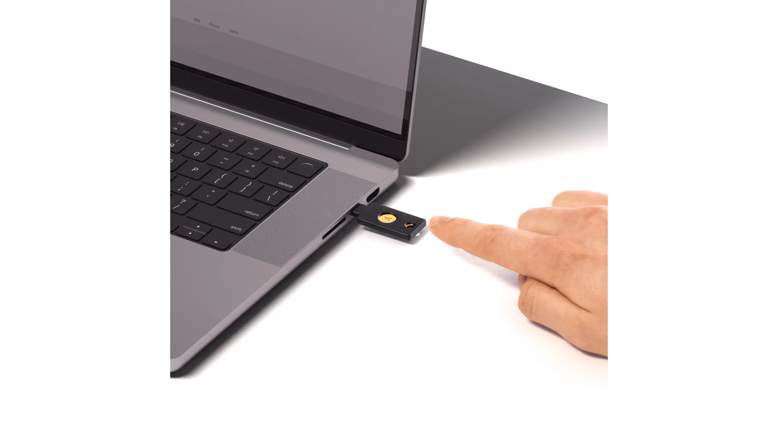 A YubiKey 5C NFC connected to a laptop, with a finger on the touch contact